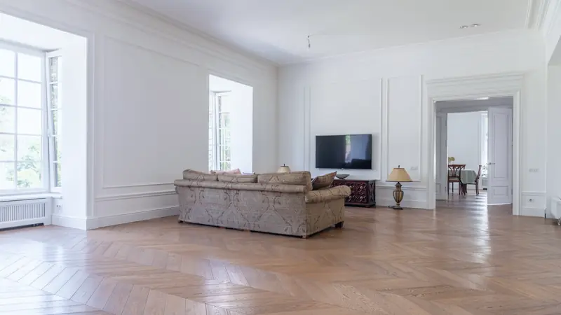 Grand séjour aux murs moulurés et parquet en point de Hongrie, éclairé par de hautes fenêtres
