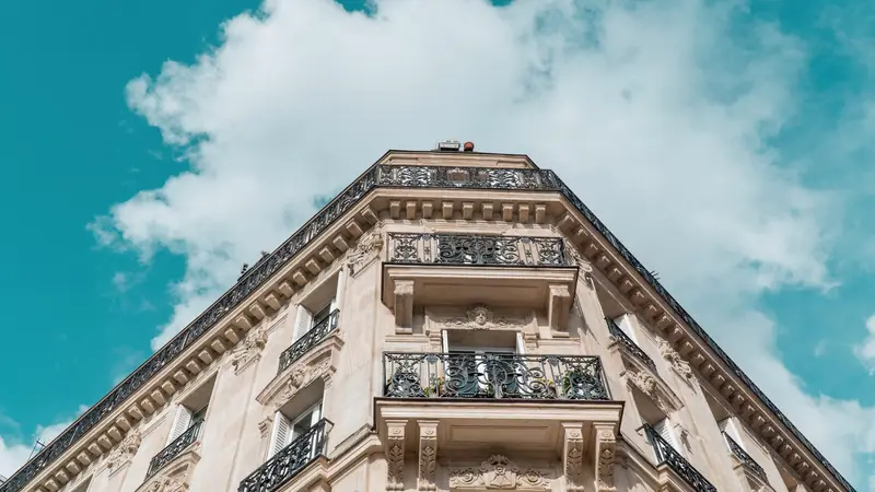 Angle d'un immeuble parisien en pierre de taille aux balcons en fer forgé, vu en contre-plongée sous un ciel bleu