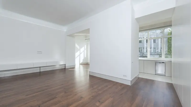 Appartement vide et lumineux aux murs blancs, parquet foncé, cuisine ouverte et grandes fenêtres