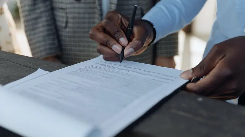 Main tenant un stylo au-dessus d'un contrat imprimé posé sur une table, visages hors cadre