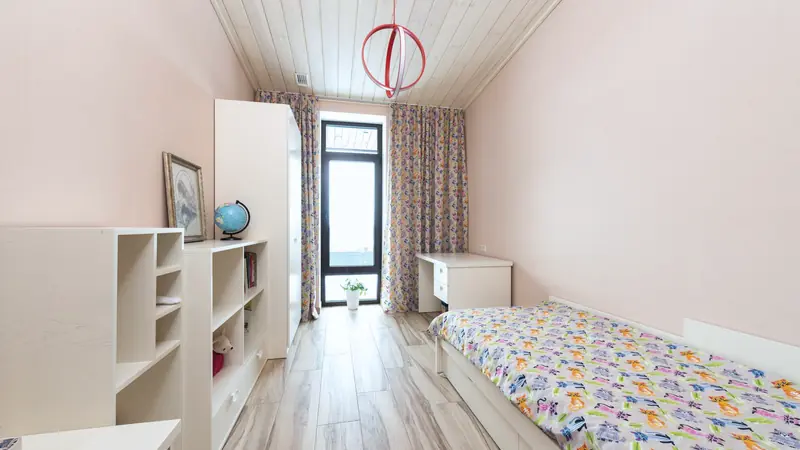 Chambre d'enfant étroite et lumineuse avec un lit simple, des étagères, un bureau et une porte-fenêtre