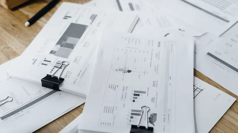 Liasses de documents chiffrés retenues par des pinces, étalées sur une table en bois
