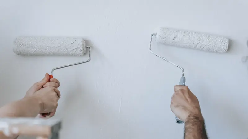 Deux mains repeignant un mur en blanc au rouleau