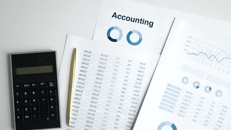 Calculatrice noire, stylo doré et tableaux de chiffres imprimés posés sur un bureau blanc