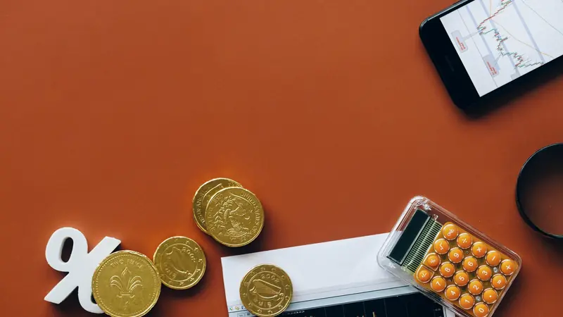 Pièces de monnaie, signe pourcentage, calculatrice orange et graphique financier sur un fond rouge brique