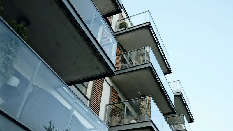 Balcons vitrés d'un immeuble résidentiel récent vus en contre-plongée sous un ciel clair