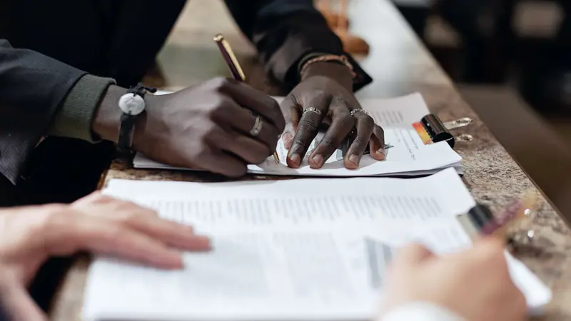 Deux mains signant un document posé sur un comptoir face à une autre personne qui tient des feuilles