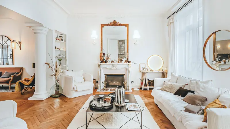 Salon d'appartement ancien meublé avec cheminée en marbre, miroir doré, moulures et parquet en point de Hongrie