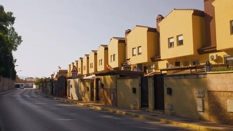 Rangée de maisons mitoyennes jaunes à toits de tuiles le long d'une rue espagnole en fin de journée