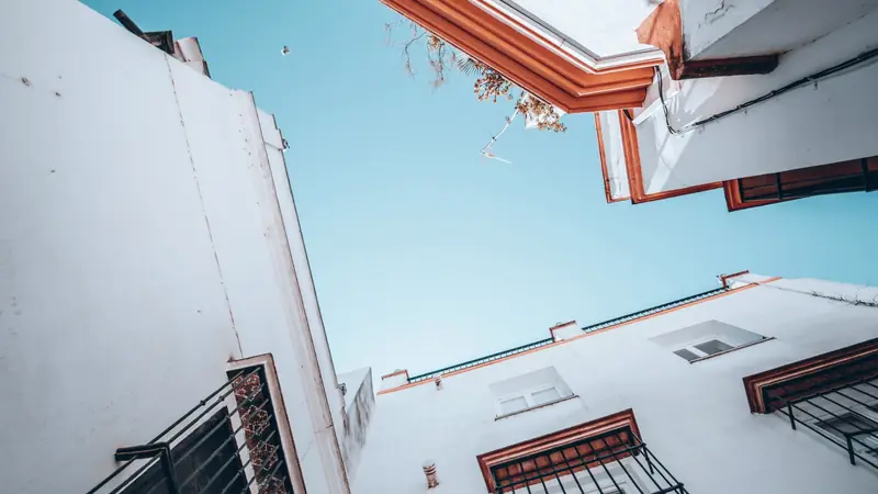 Façades blanches à fenêtres grillagées et corniches ocre d'une ruelle andalouse, vues en contre-plongée sous un ciel bleu