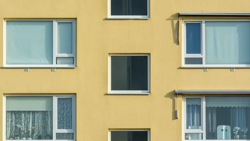Façade jaune d'un immeuble d'habitation avec ses fenêtres blanches et deux auvents