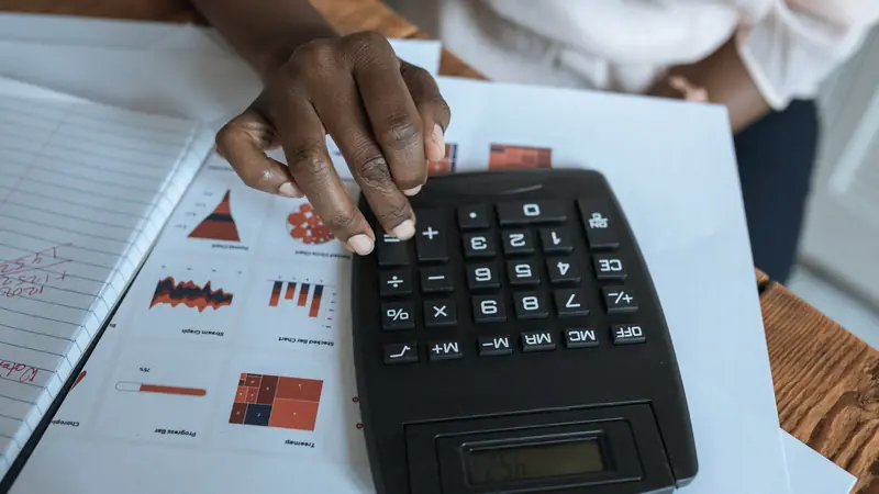 Main tapant sur une calculatrice posée sur des feuilles de graphiques et un cahier annoté