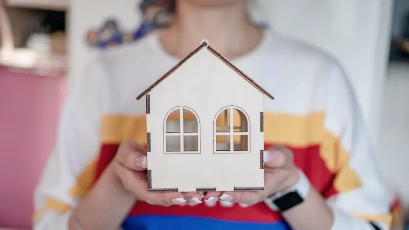 Mains tenant une petite maison en bois découpé aux fenêtres cintrées