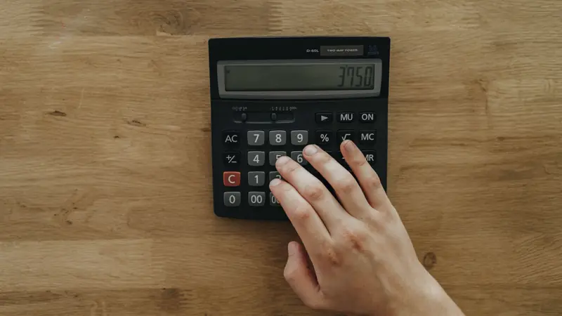 Main posée sur une calculatrice de bureau noire, sur une table en bois