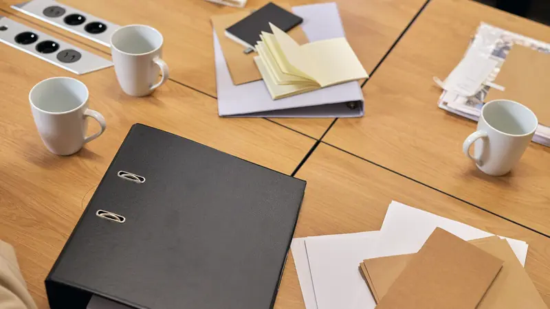 Table de réunion en bois avec classeur noir, carnets, dossiers et tasses à café