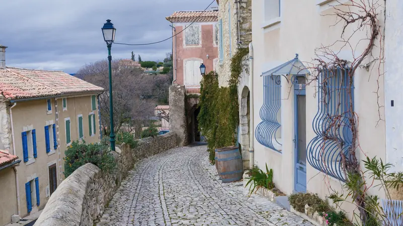 Ruelle pavée d'un village provençal bordée de maisons en pierre aux volets bleus et verts